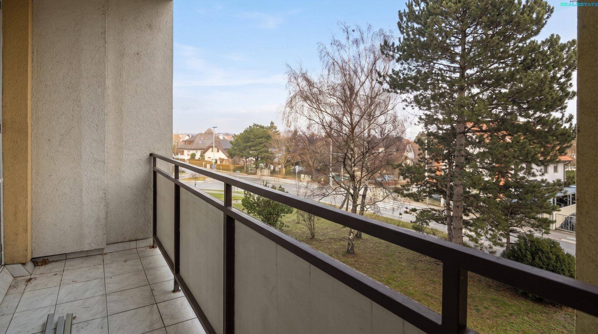Balkon mit Fliesenboden und Blick auf die Straße und umliegende Bäume.