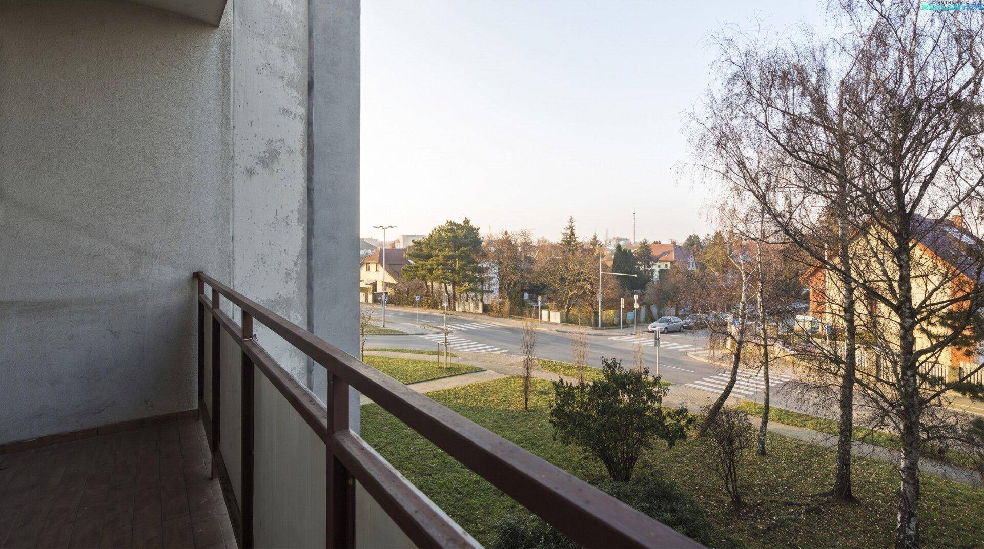 Balkon mit Fliesenboden und weitem Blick über die Straße und die grüne Umgebung.