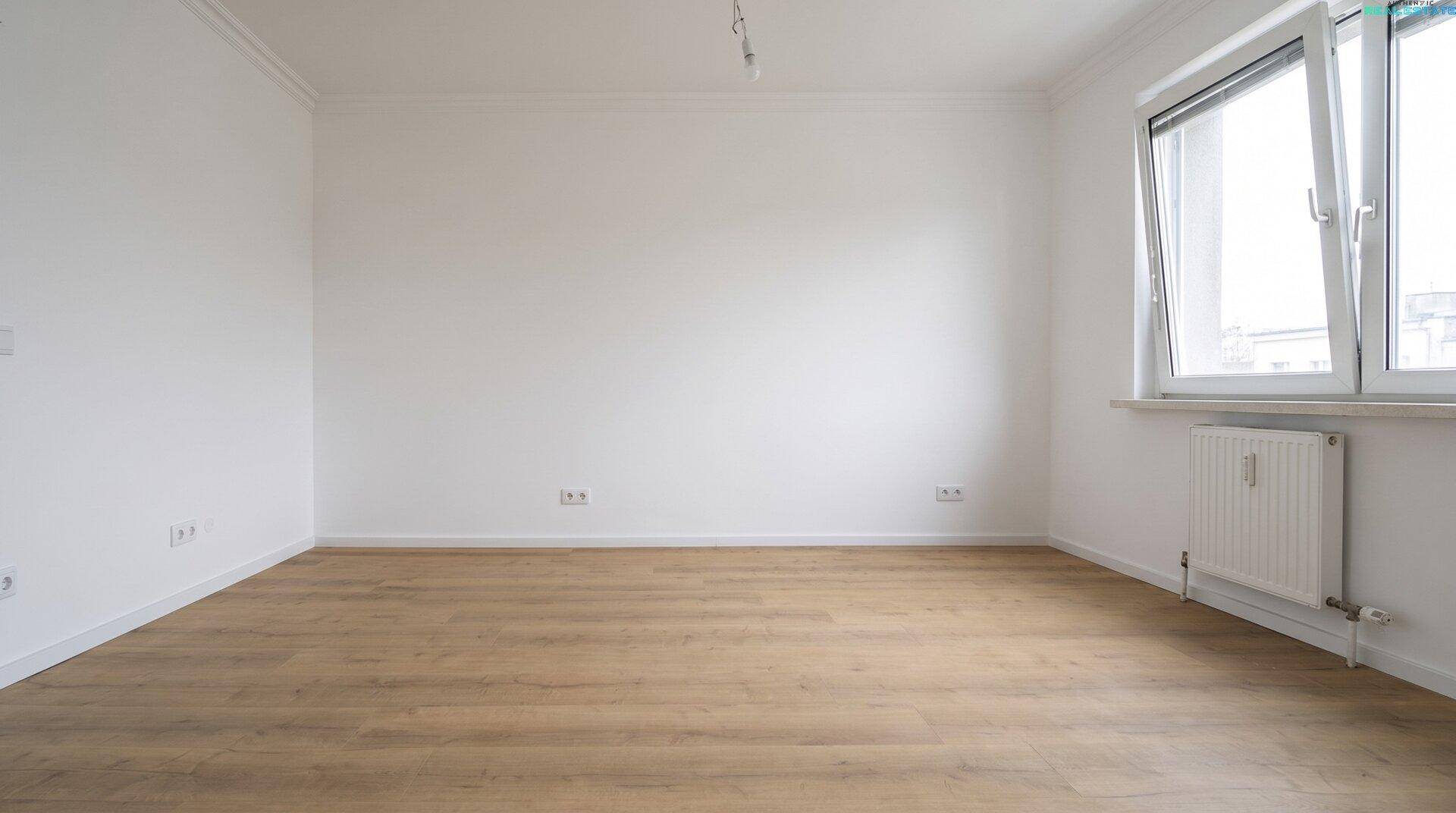 Leeres Schlafzimmer mit hellem Holzboden und einem großen Fenster für viel Tageslicht.