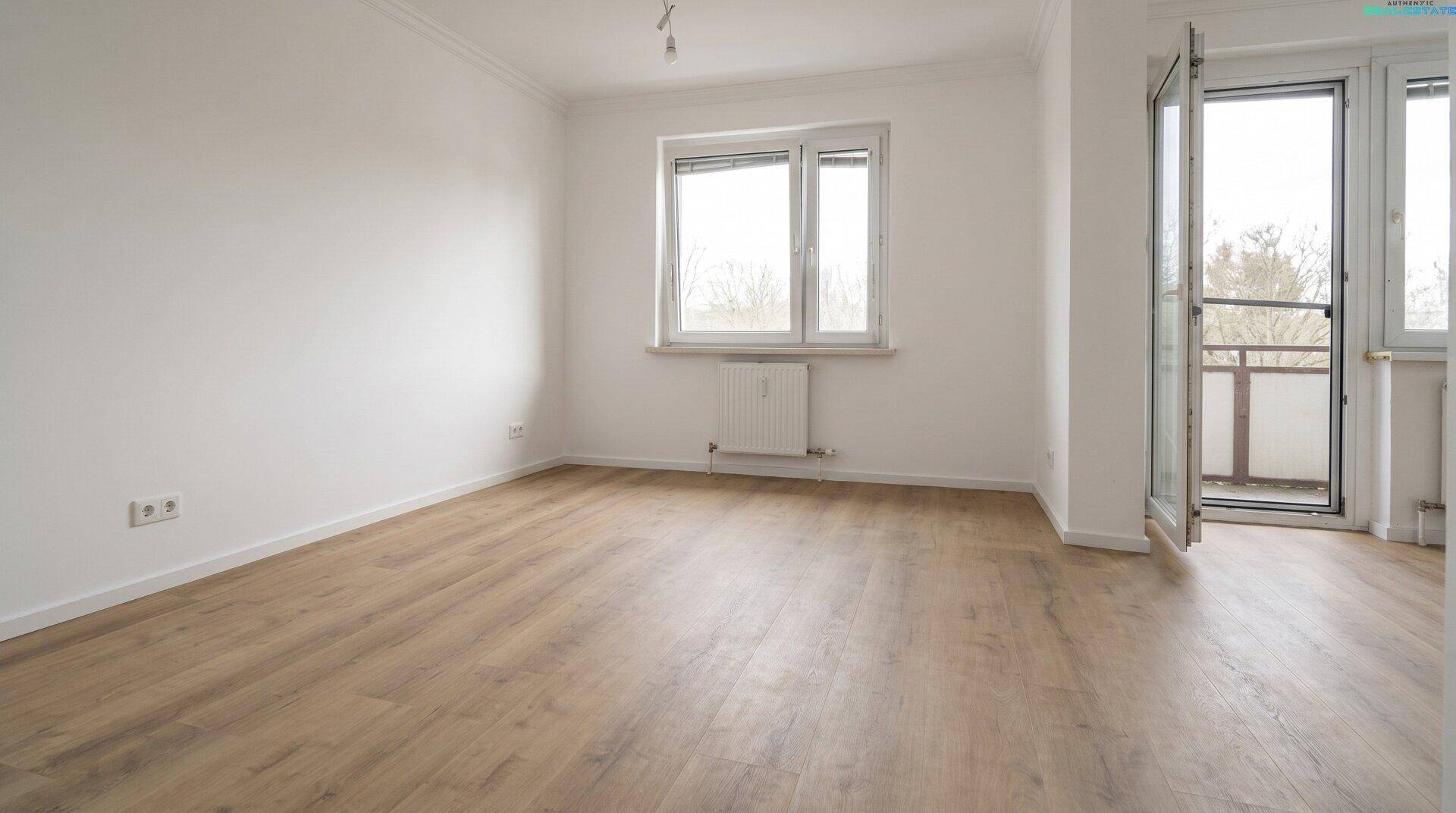 Heller Raum mit Holzboden, weißen Wänden und direktem Zugang zu einem Balkon.