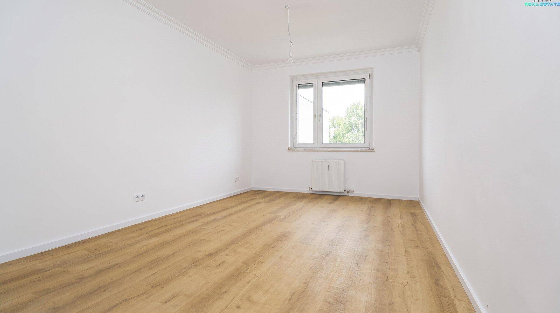 Leeres Schlafzimmer mit hellem Holzboden und einem Fenster, das viel Tageslicht hereinlässt.