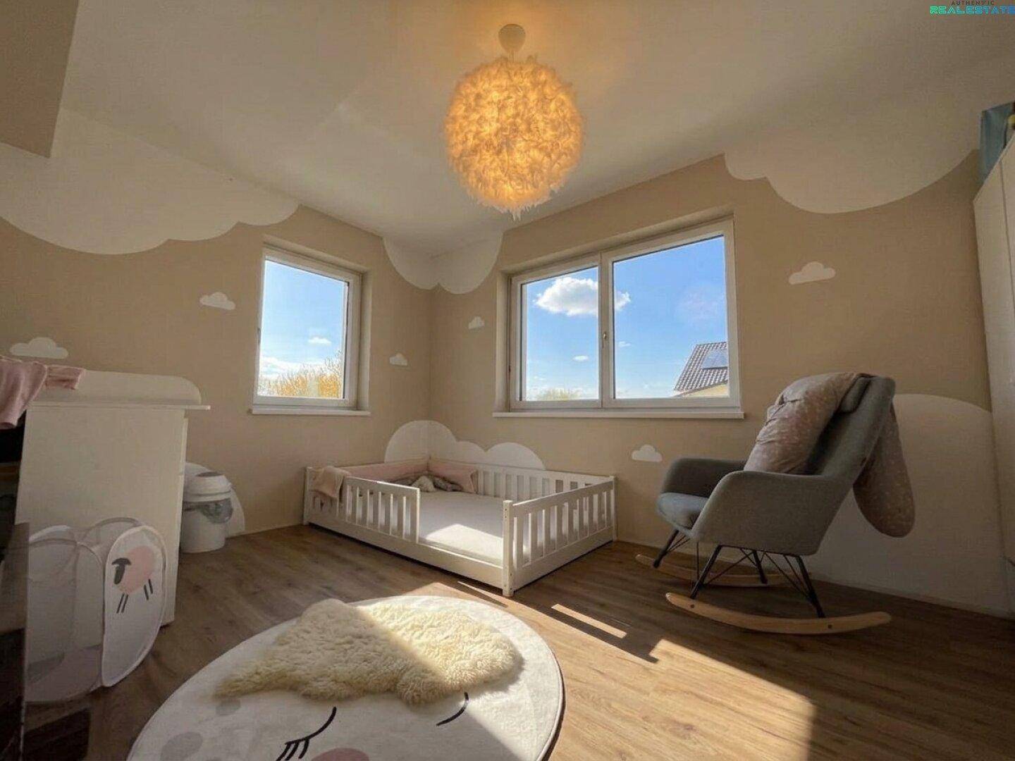Liebevoll eingerichtetes Kinderzimmer mit Babybett, Schaukelstuhl und Wolken-Wanddekoration.
