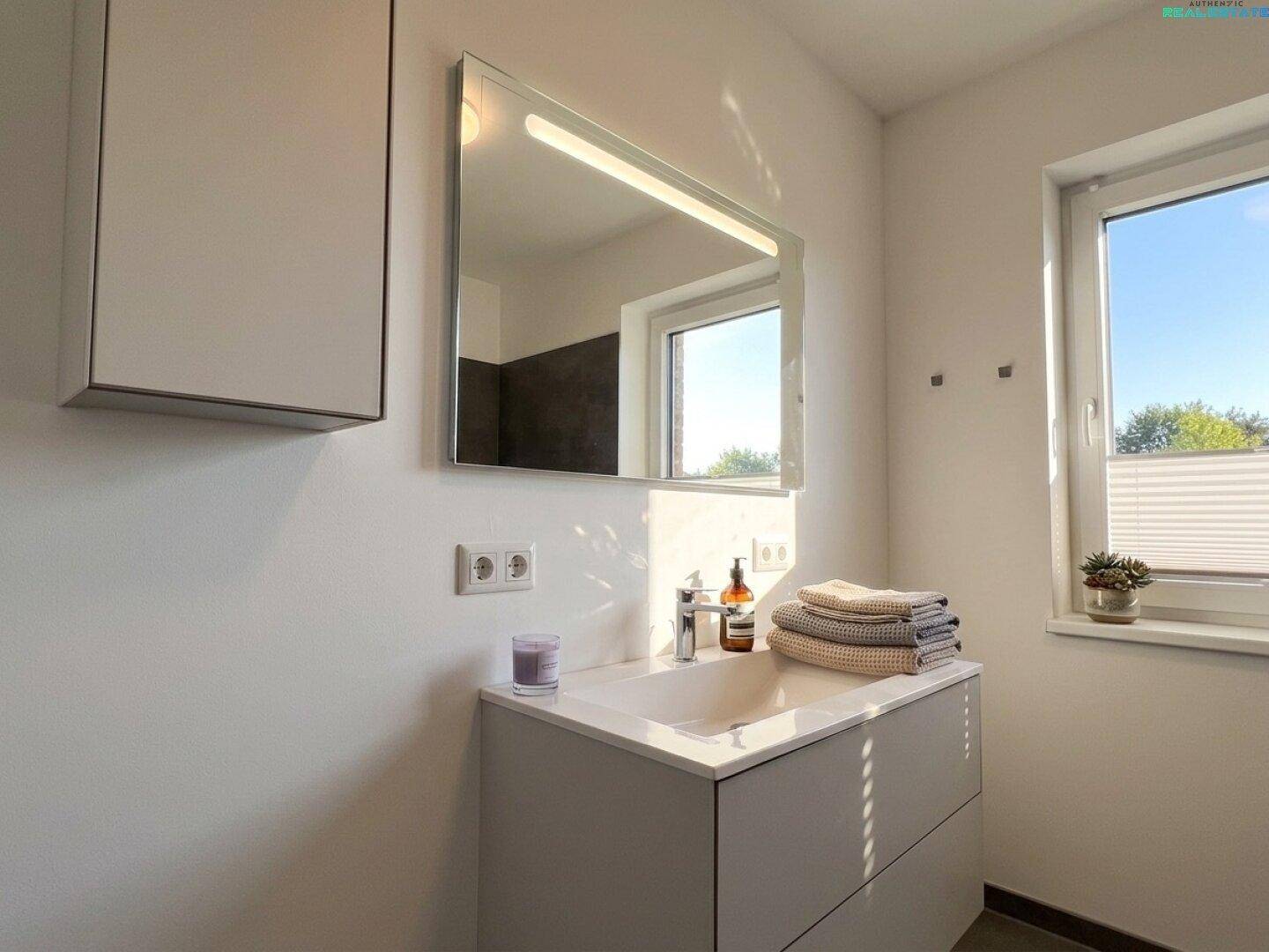 Helles Badezimmer mit modernem Waschtisch, beleuchtetem Spiegel und Fenster.