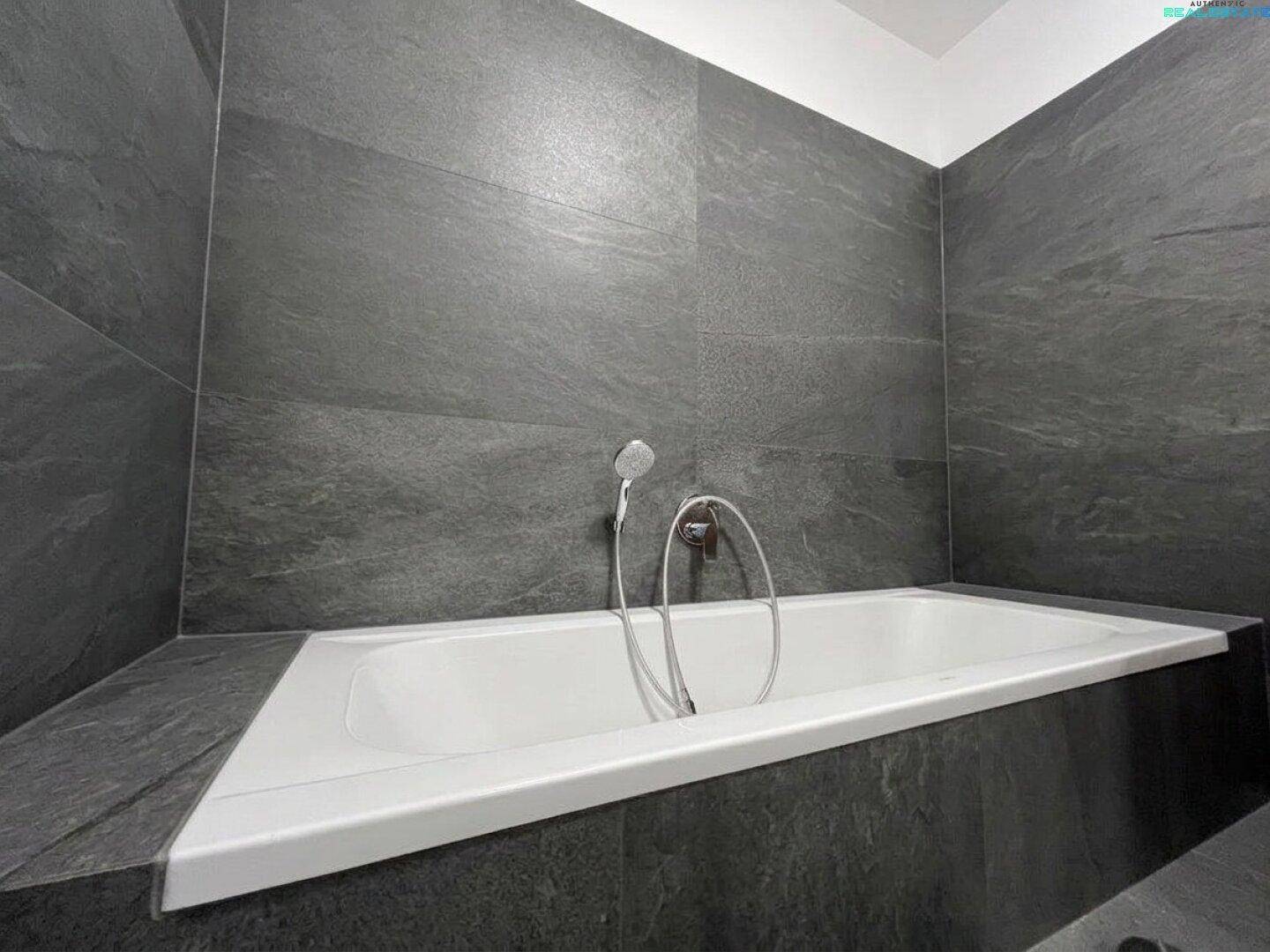 Modernes Badezimmer mit eingebauter Badewanne und eleganten dunkelgrauen Fliesen.