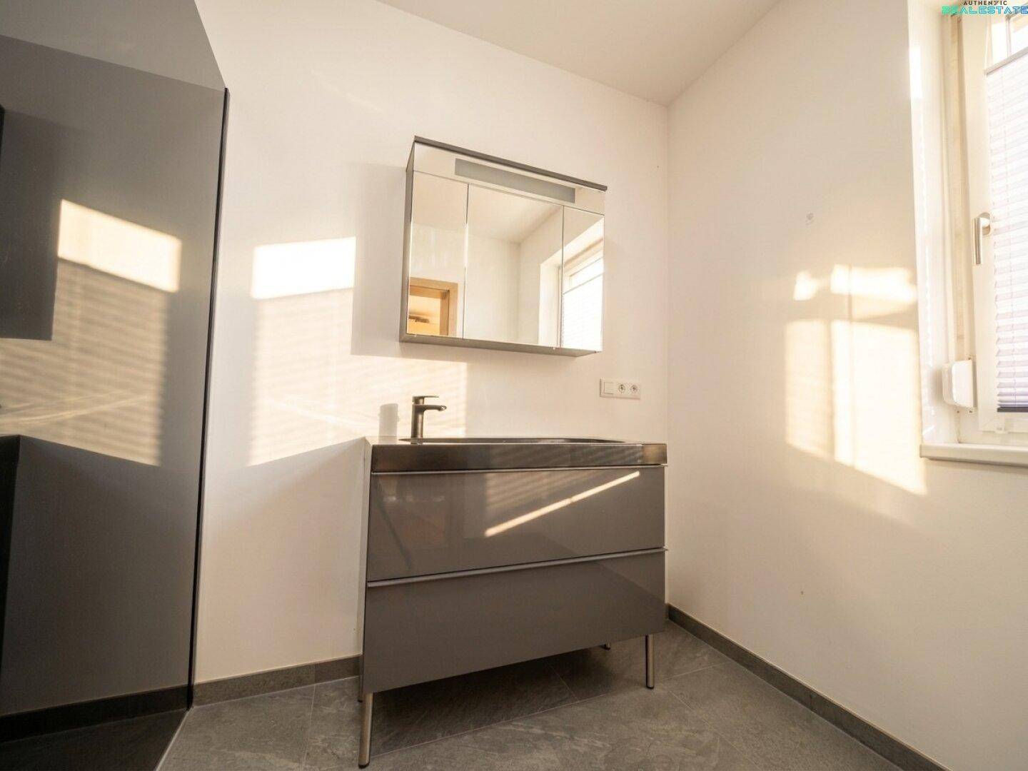Modernes Badezimmer mit Einzelwaschbecken, Spiegelschrank und Fenster für natürliches Tageslicht.