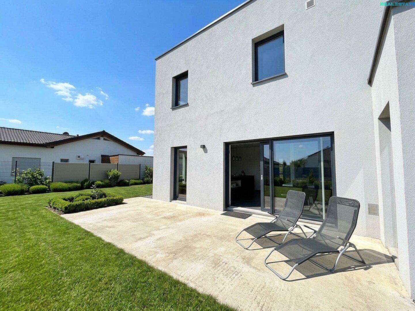 Sonniger Außenbereich mit großer Terrasse, Liegestühlen und gepflegtem Rasen.