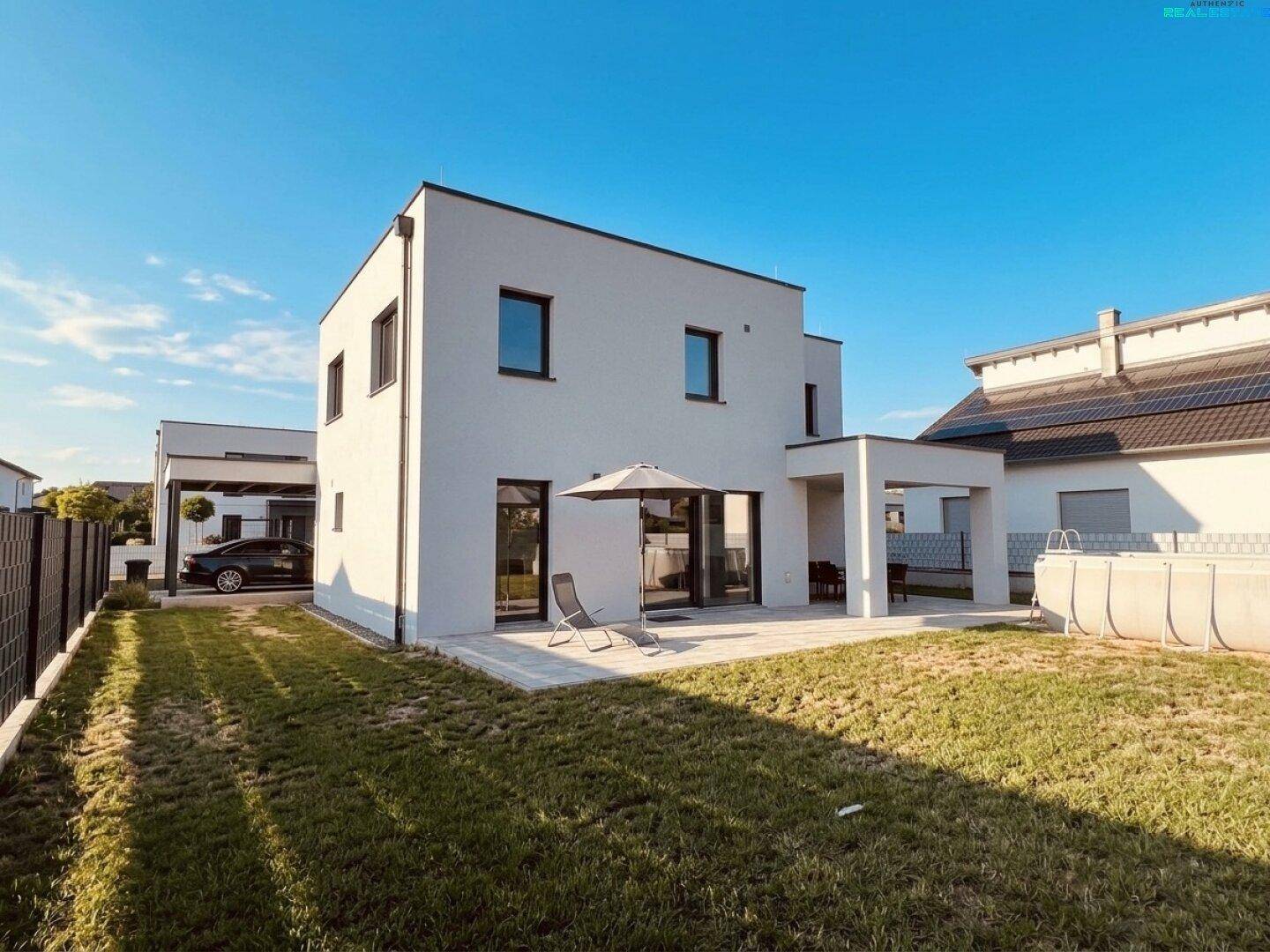 Modernes Einfamilienhaus von der Gartenseite mit Terrasse, Rasen und Pool.