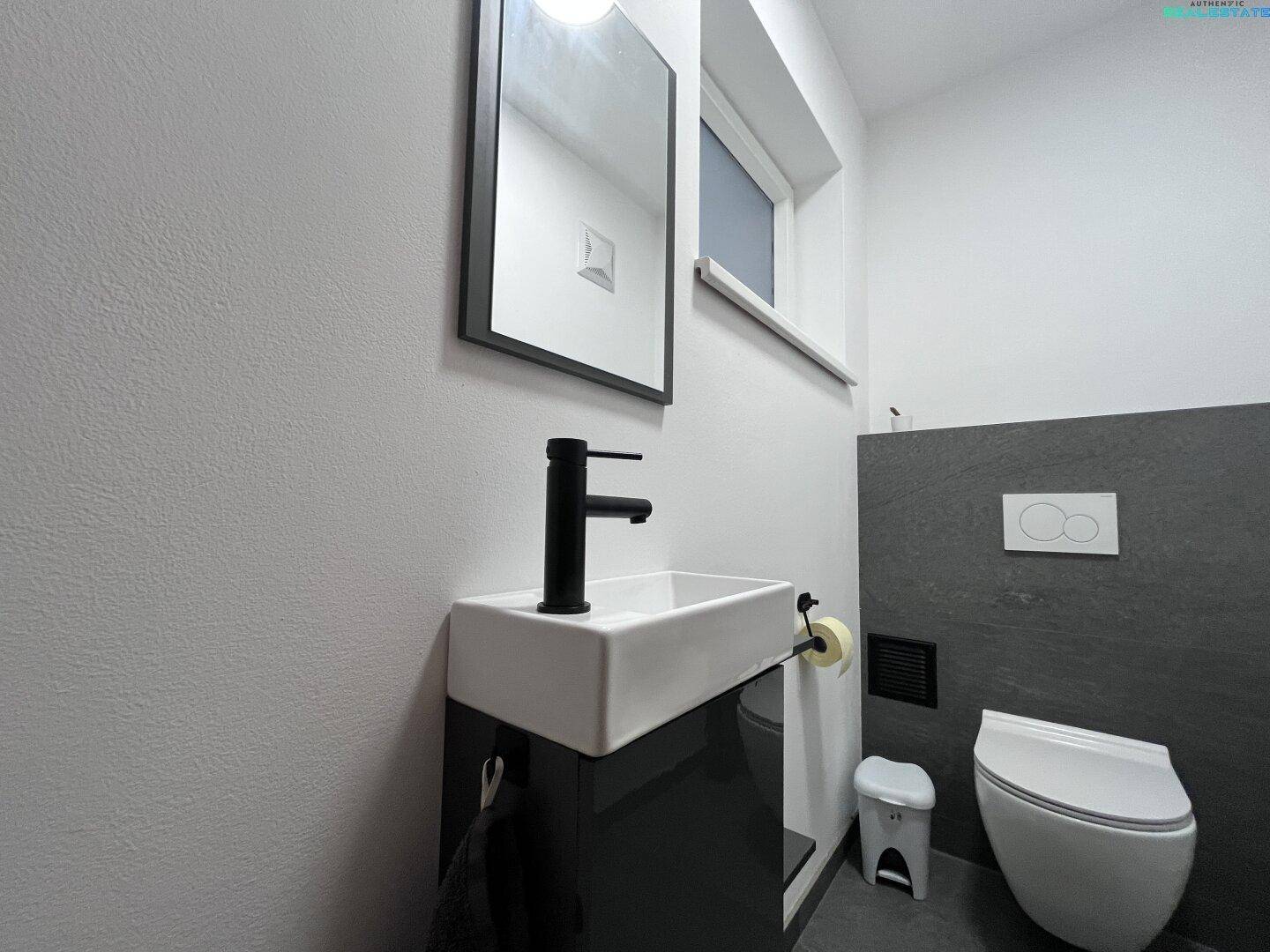 Modernes Gäste-WC mit kleinem Waschbecken, Spiegel und wandhängendem WC.