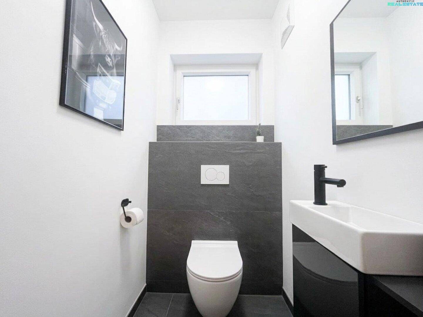 Modernes Gäste-WC mit dunklen Fliesen, wandhängendem WC und kleinem Waschbecken, minimalistisches Design.