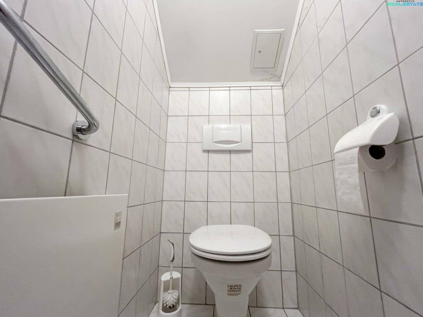 Separates WC mit weißen Fliesen, Wand-WC und Haltegriff für Komfort.