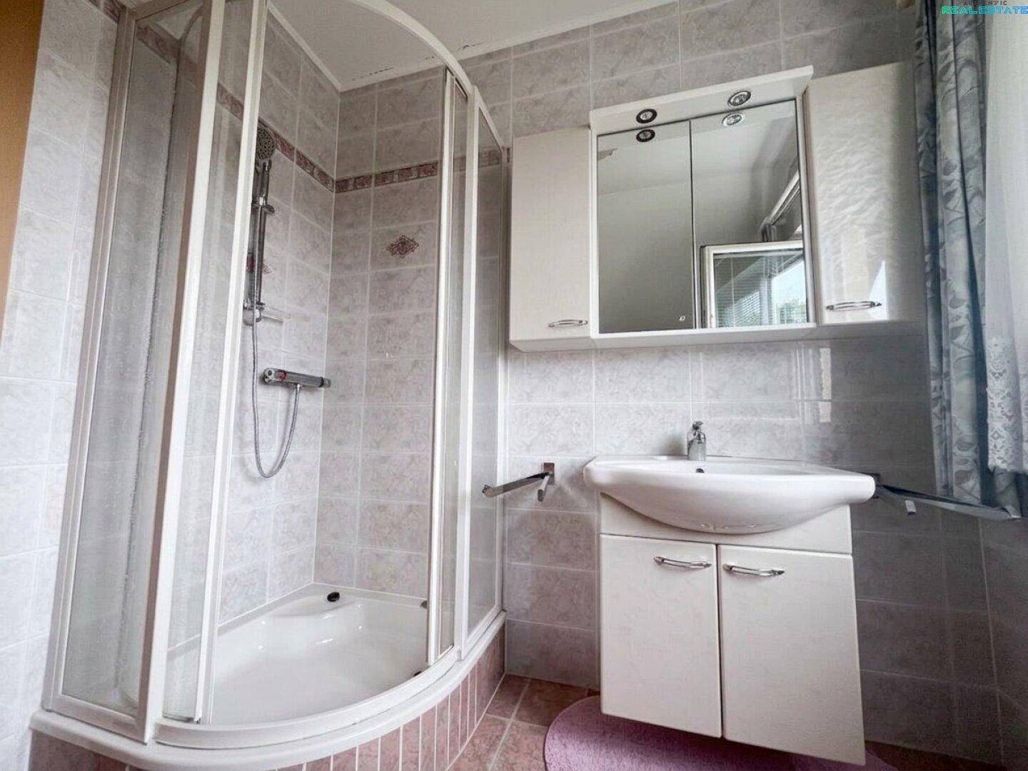 Badezimmer mit Duschkabine, Waschbeckenunterschrank und Spiegelschrank in hellen Fliesen.
