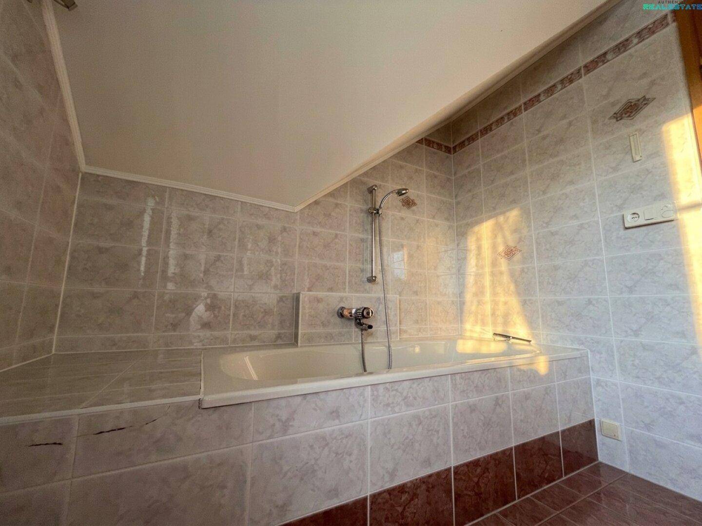 Badezimmer mit eingebauter Badewanne und gefliesten Wänden unter einer Dachschräge.