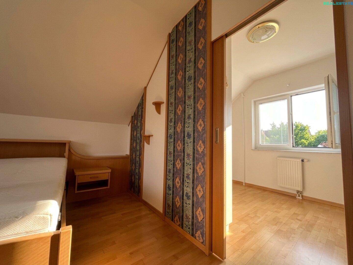 Schlafzimmer mit Parkettboden, gemusterter Tapete und Fenster mit Blick ins Grüne.
