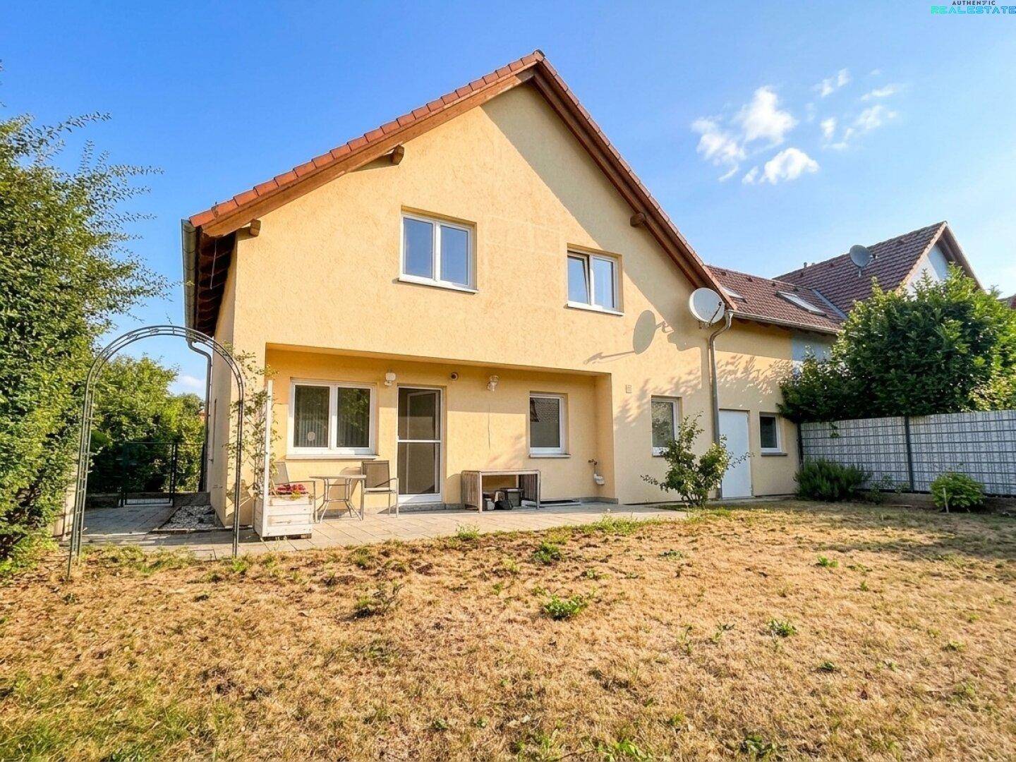 Rückansicht des Hauses mit Terrasse und trockenem Rasenbereich unter klarem Sommerhimmel.