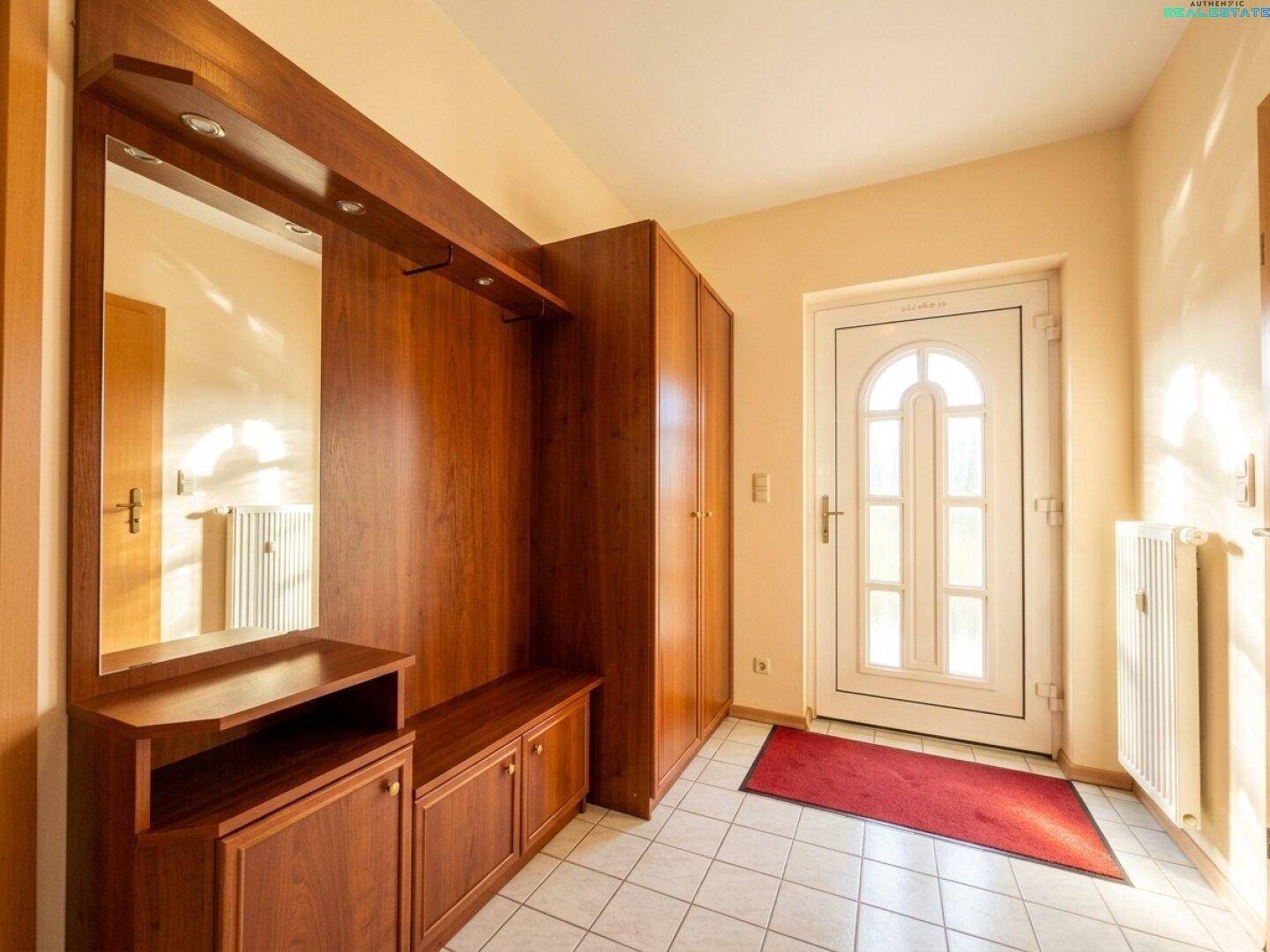Heller Eingangsbereich mit Fliesenboden, Garderobe aus Holz und weißer Haustür.