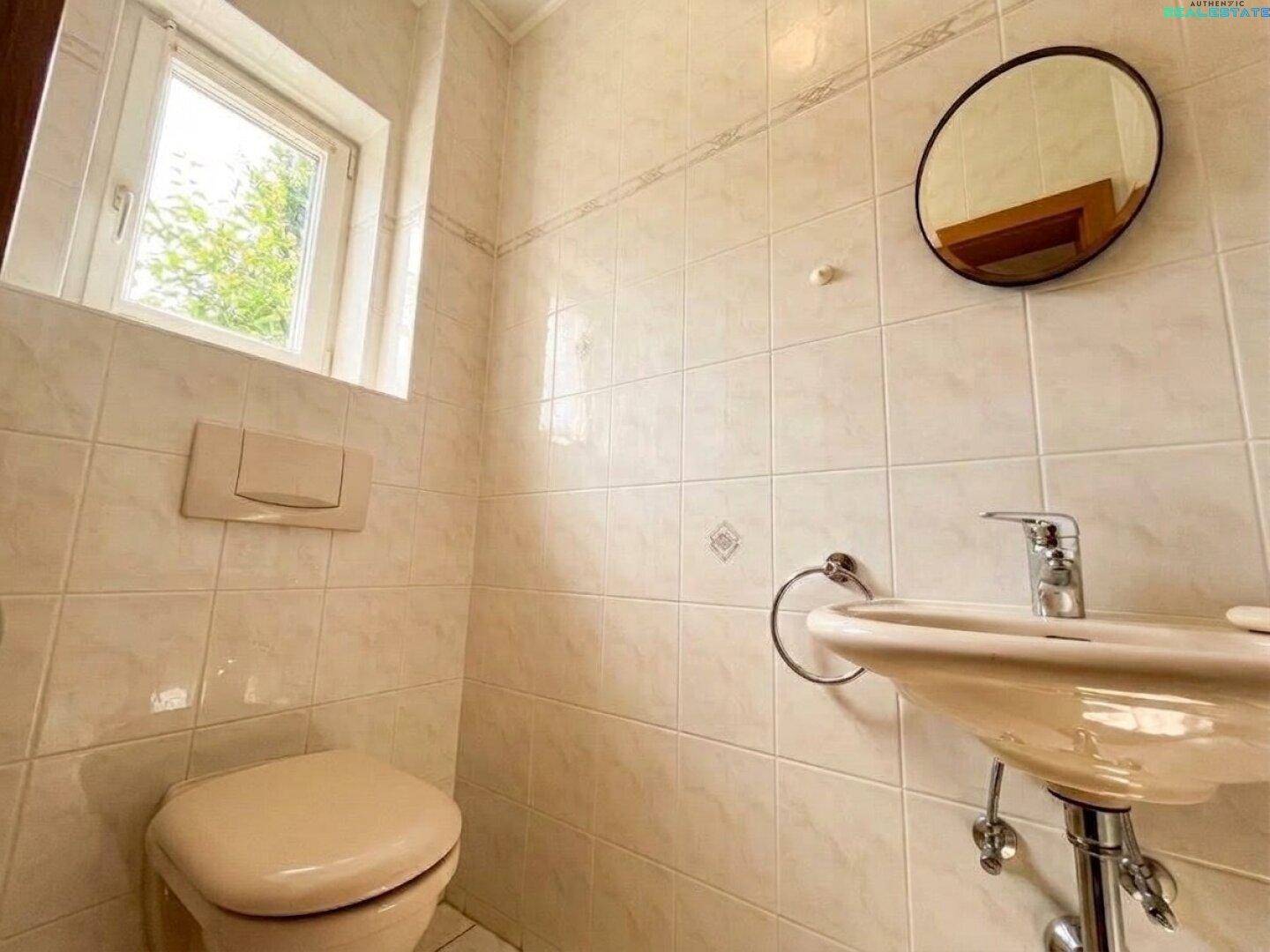 Kleines Gäste-WC mit hellen Fliesen, Fenster und einfacher Ausstattung.