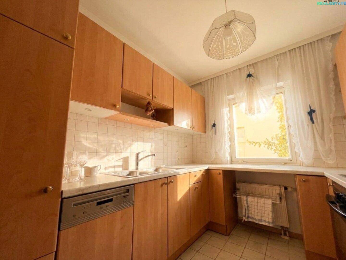 Funktionale Küche mit hellen Holzschränken, Fliesenrückwand und Fenster mit Vorhängen.