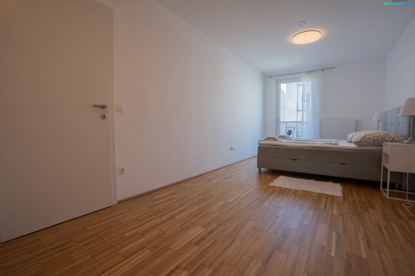 Helles Schlafzimmer mit Bett, Holzboden und Fenster mit Heizkörper.