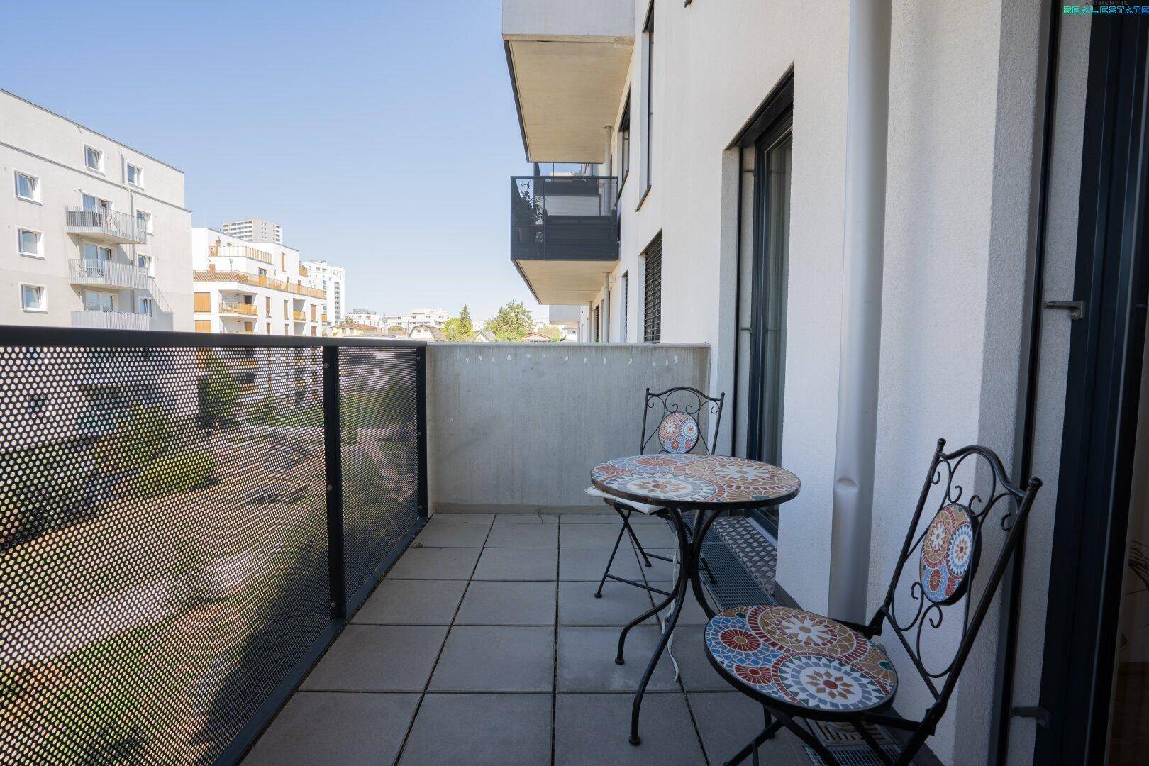 Möblierter Balkon mit Fliesenboden und Blick auf die umliegenden Gebäude und Grünflächen.