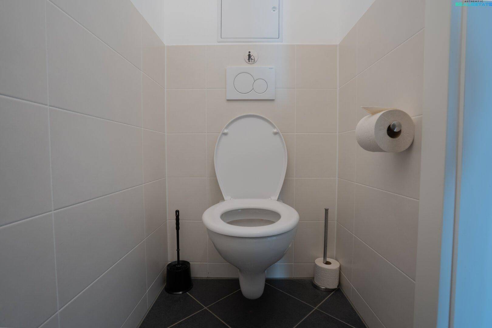 Separates WC mit Wand-WC und hellen Fliesen an den Wänden.