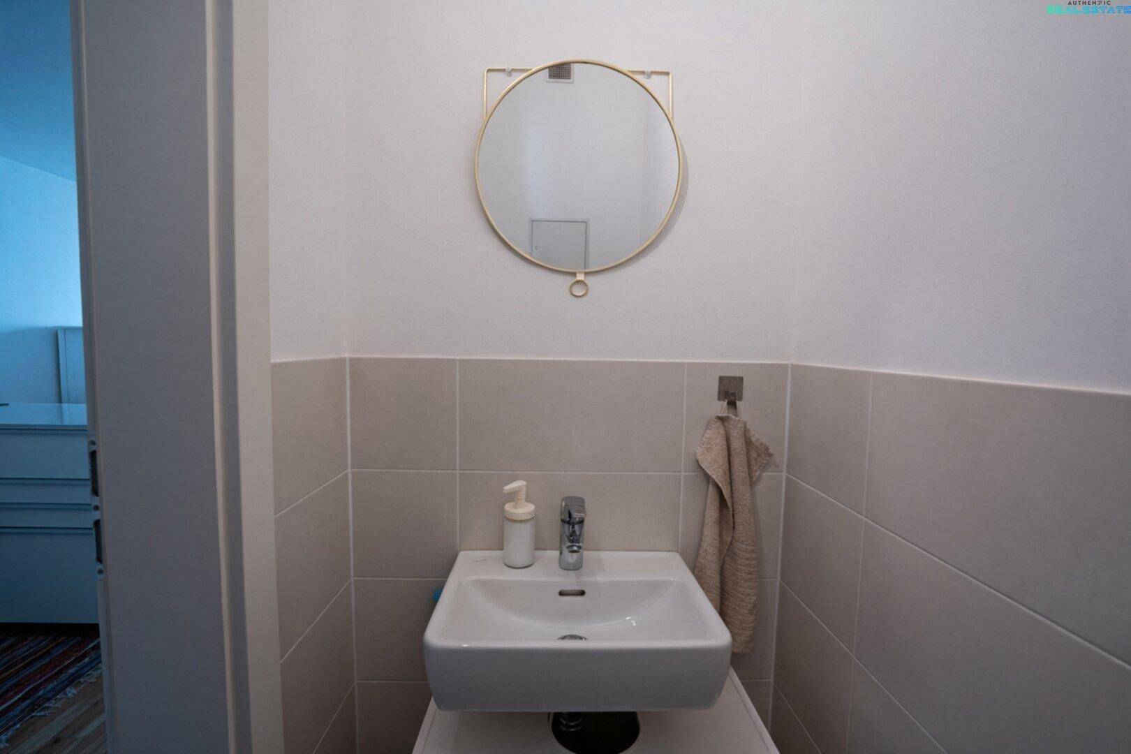Kleines Waschbecken mit rundem Spiegel in der Gästetoilette.