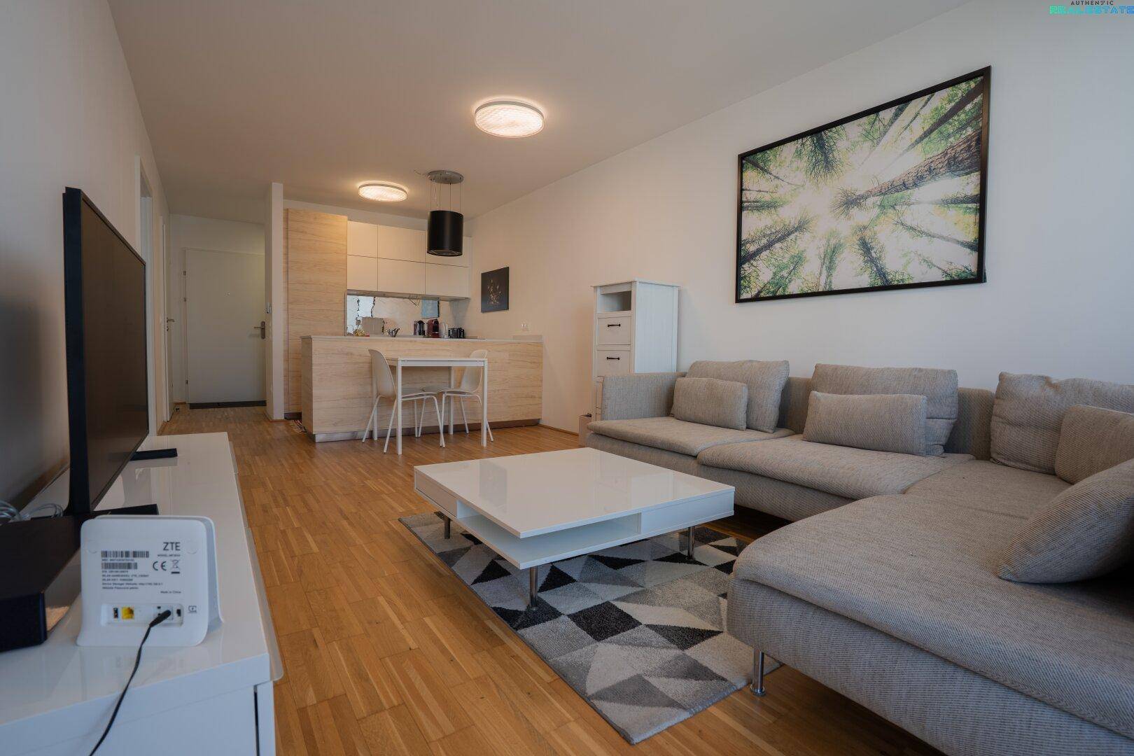 Offener Wohnbereich mit Sofa, Fernseher und Blick auf die moderne Küche mit Essbereich.