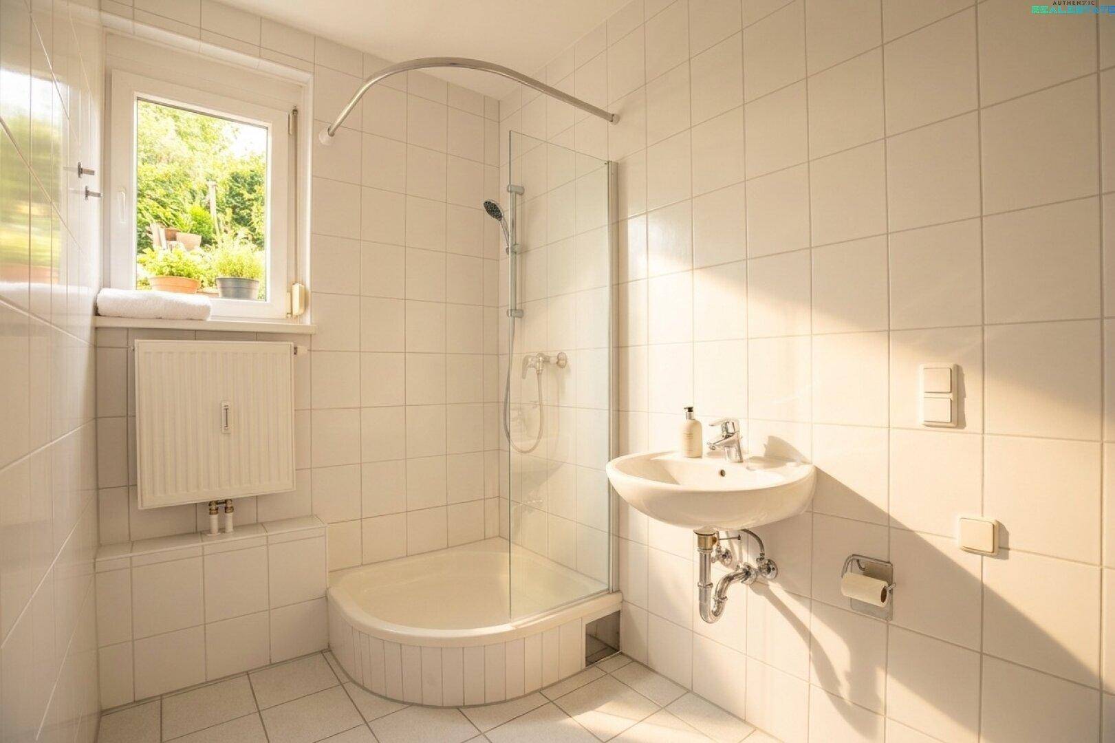 Helles Badezimmer mit weißen Fliesen, Duschkabine, Waschbecken und Fenster, durchflutet von Sonnenlicht.