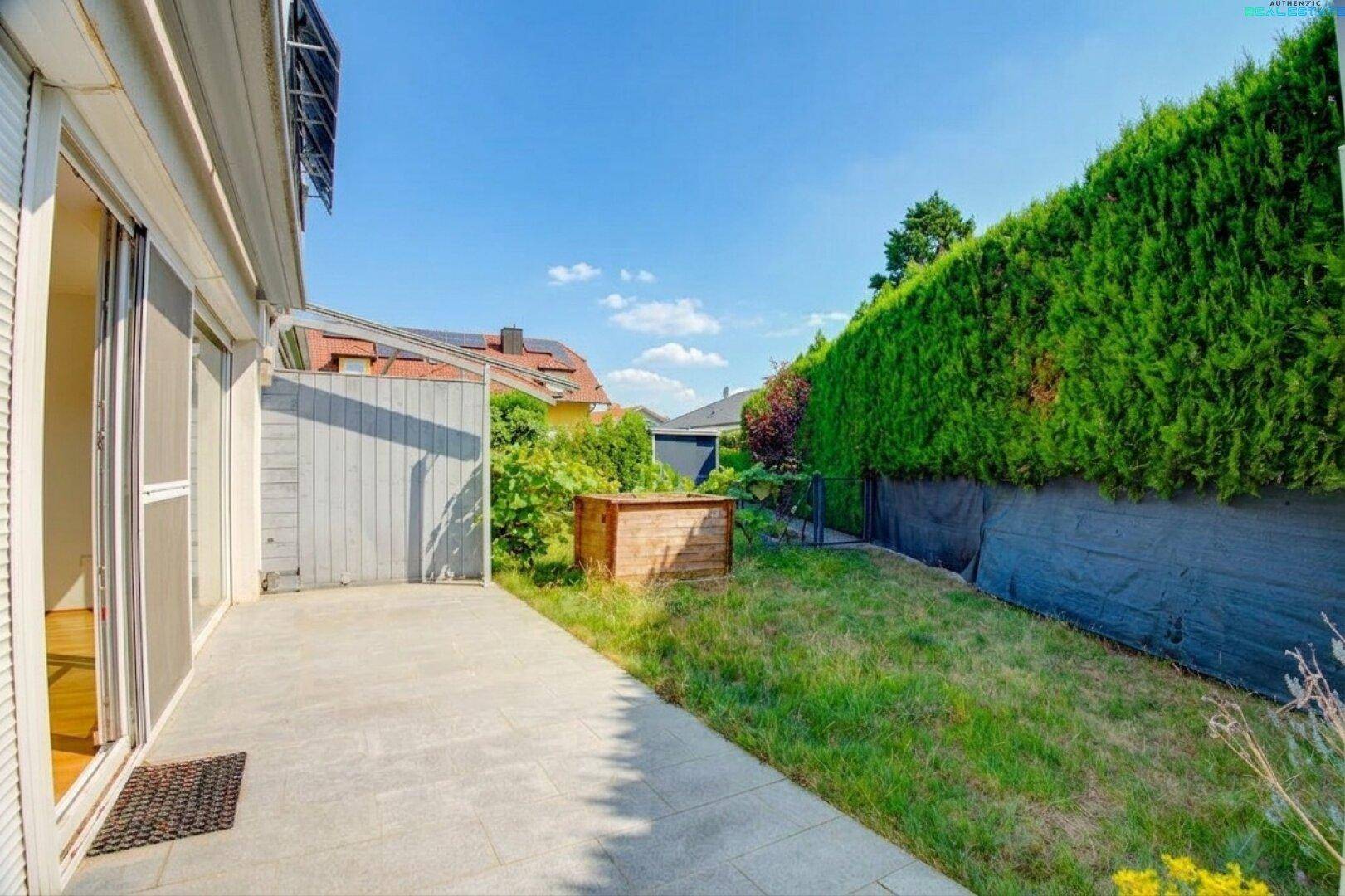 Gepflasterte Terrasse mit angrenzendem Rasenbereich und hoher Hecke im Hintergrund.