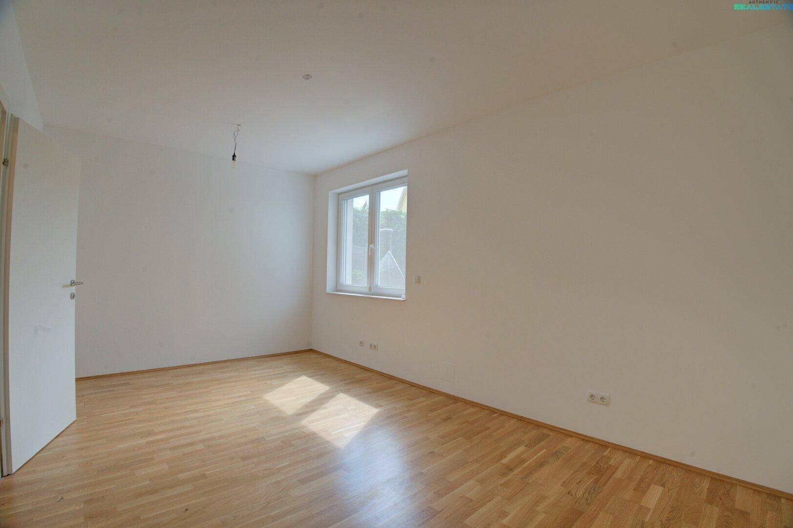 Helles Schlafzimmer mit Parkettboden und einem Fenster, das viel natürliches Licht bietet.