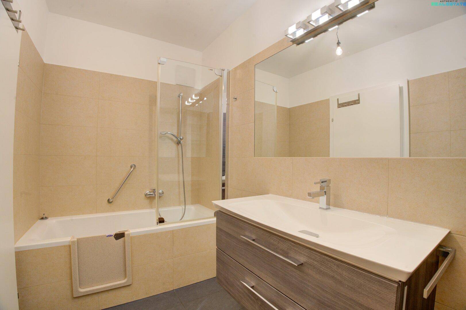 Badezimmer mit Badewanne, integrierter Dusche und Waschtisch mit Unterschrank.