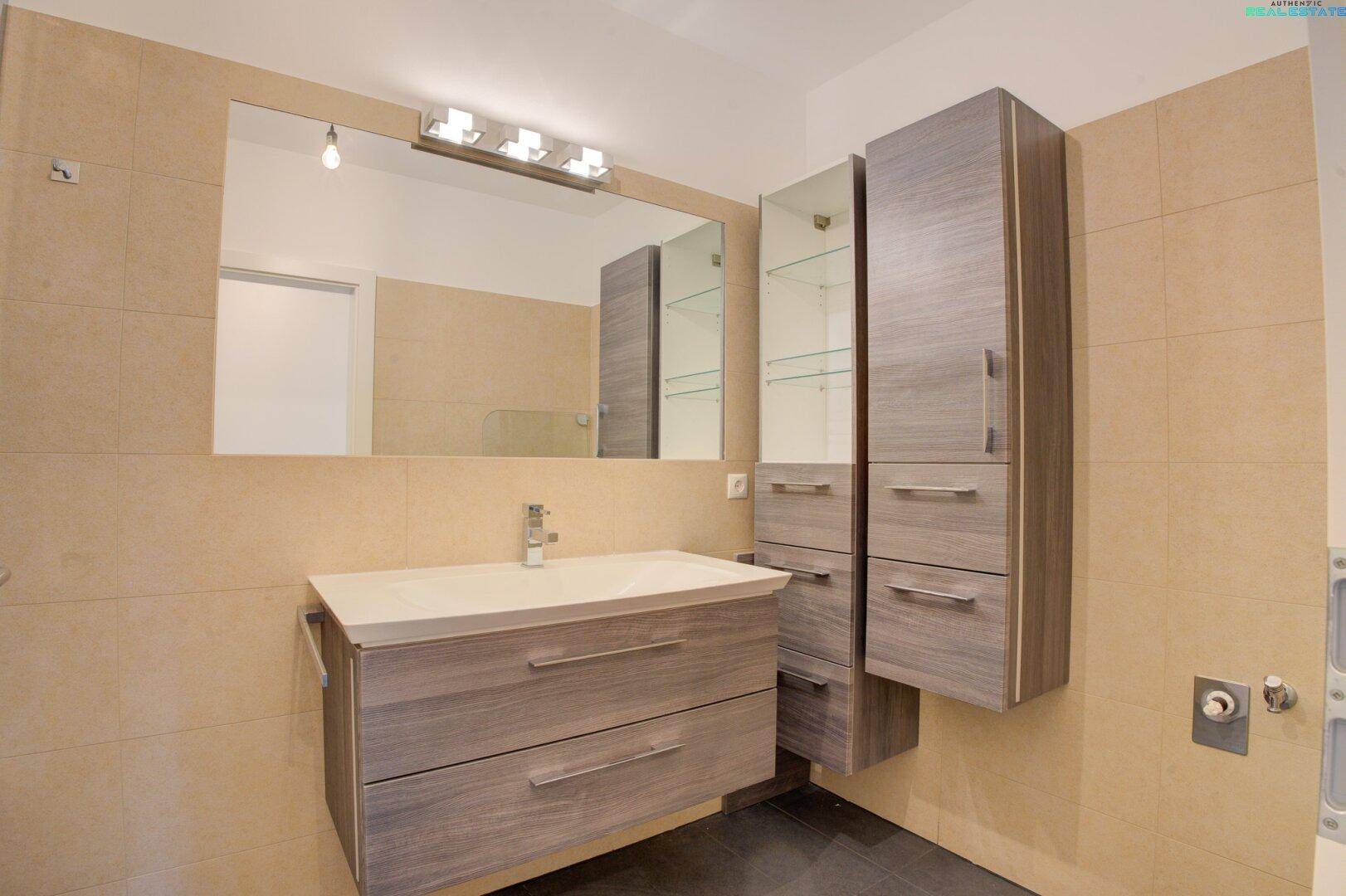 Modernes Badezimmer mit Waschtisch, großem Spiegel und praktischen Hochschränken.