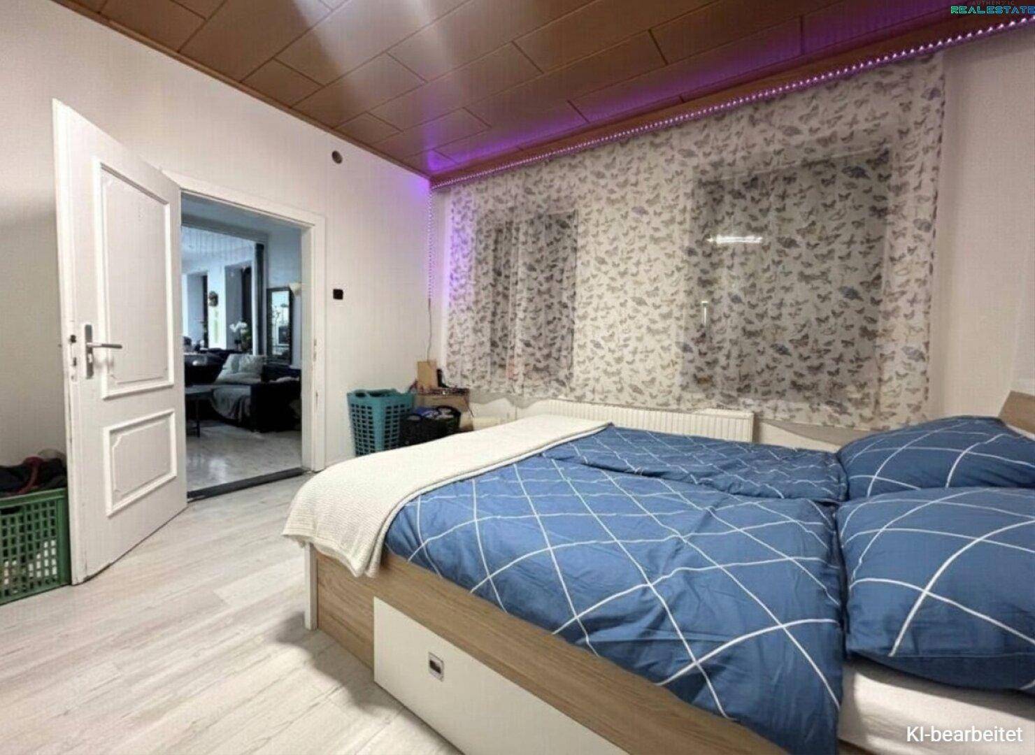 Gemütliches Schlafzimmer mit Doppelbett, blauer Bettwäsche und einer Holzpaneeldecke, verbunden mit dem Wohnbereich.