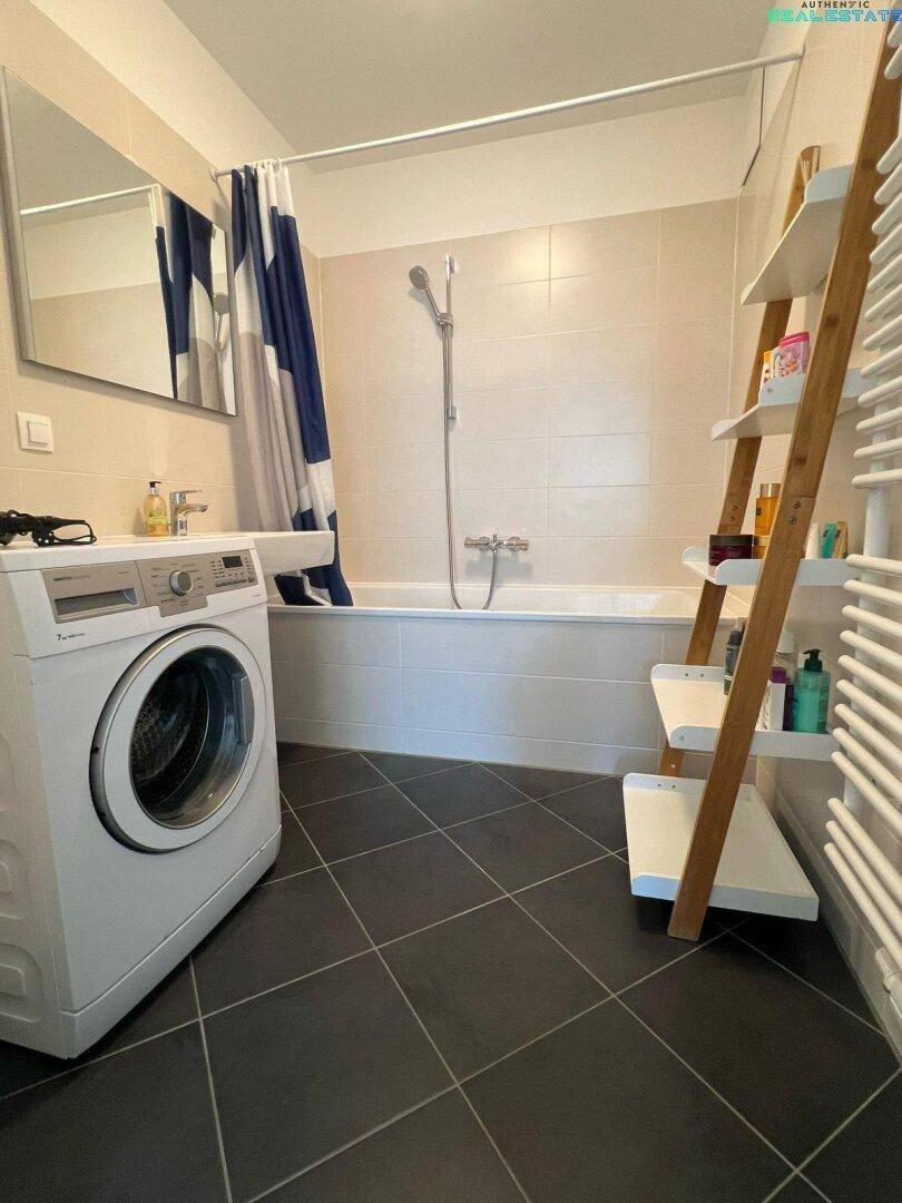 Funktionales Badezimmer mit Badewanne, Duschvorhang, Waschmaschine und dunklen Bodenfliesen.