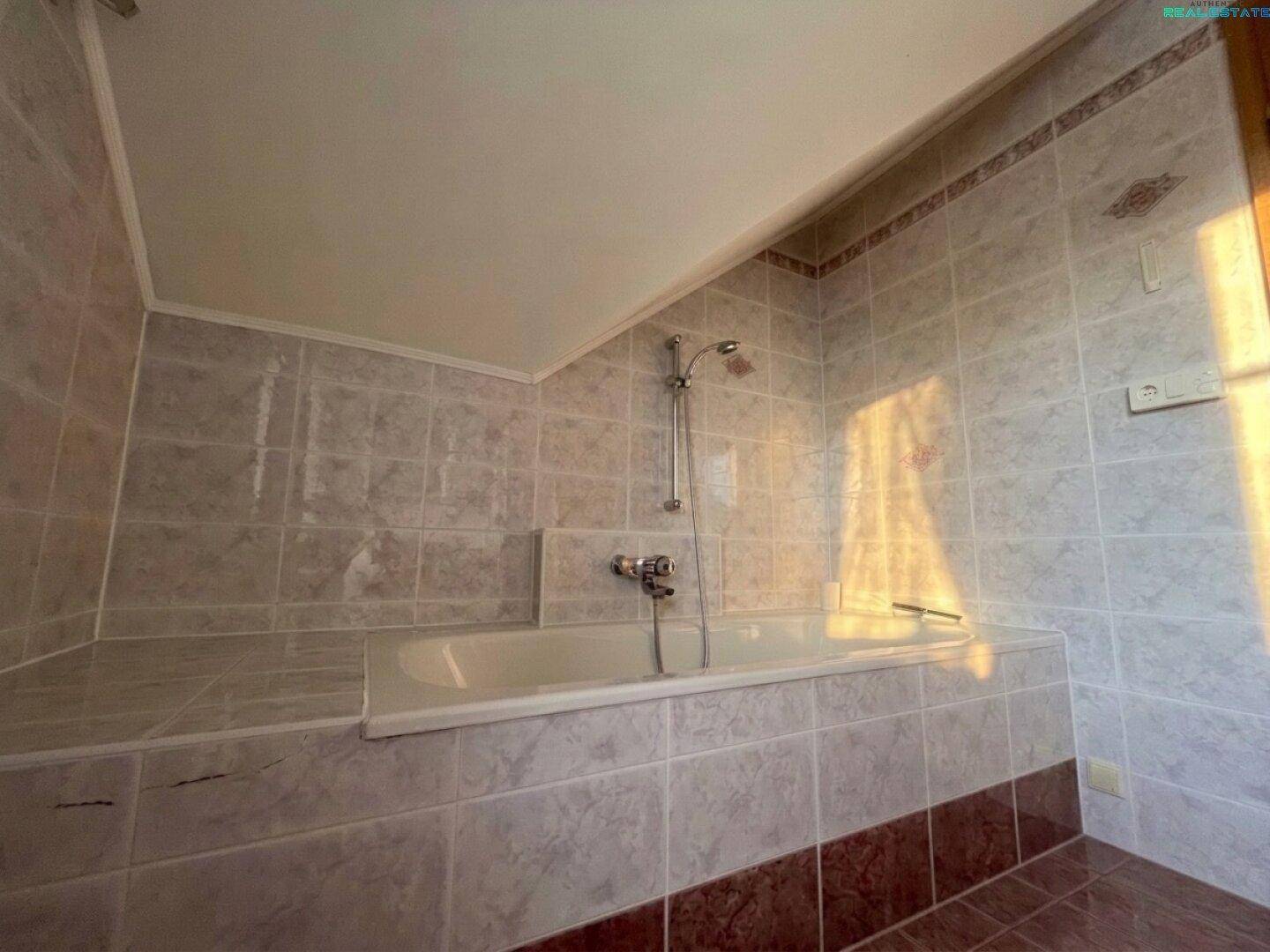 Badezimmer mit eingebauter Badewanne und gefliesten Wänden in hellen und dunklen Tönen.