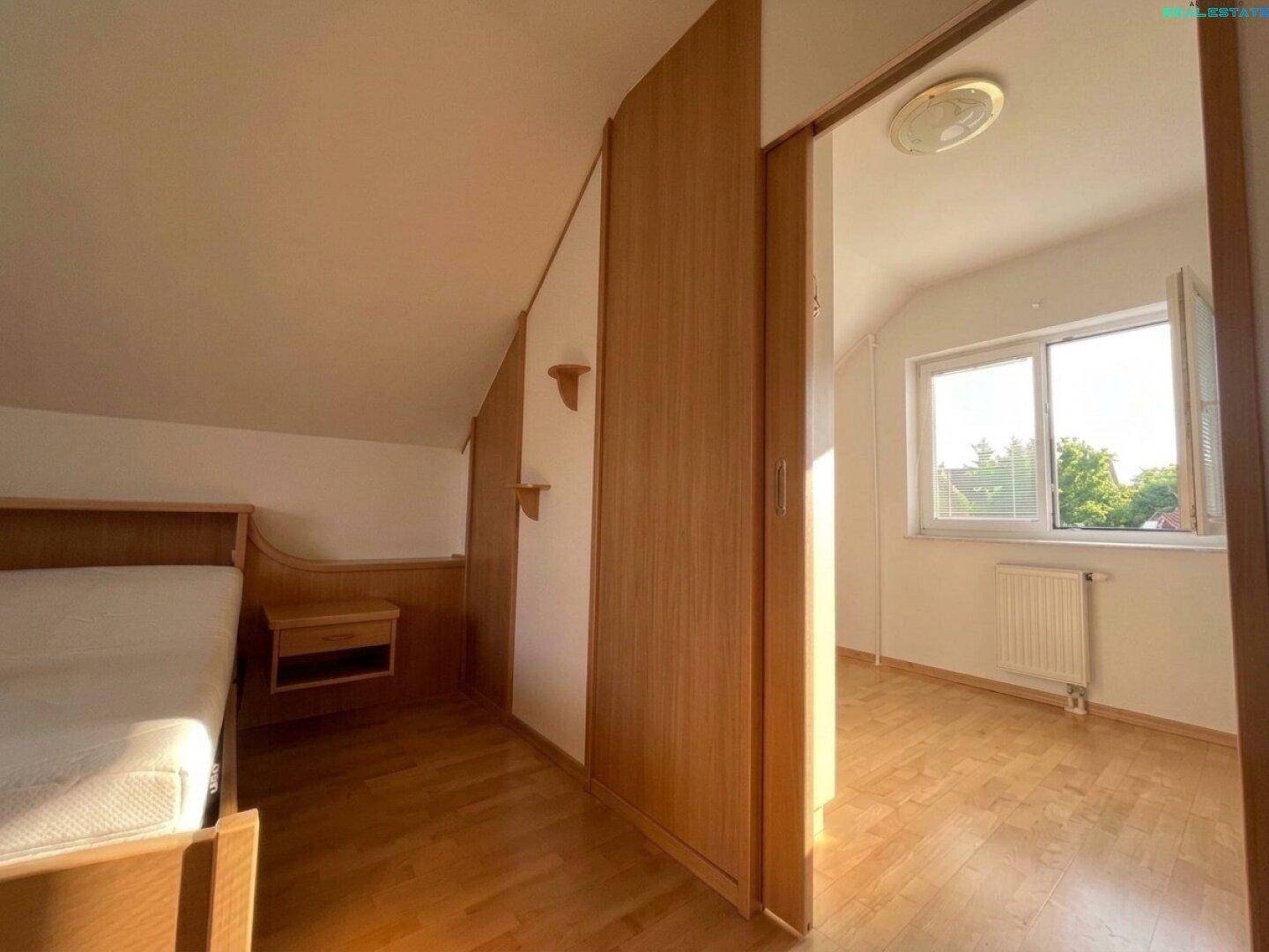 Schlafzimmer im Dachgeschoss mit Holzboden, Dachschräge und Fenster mit Blick ins Grüne.