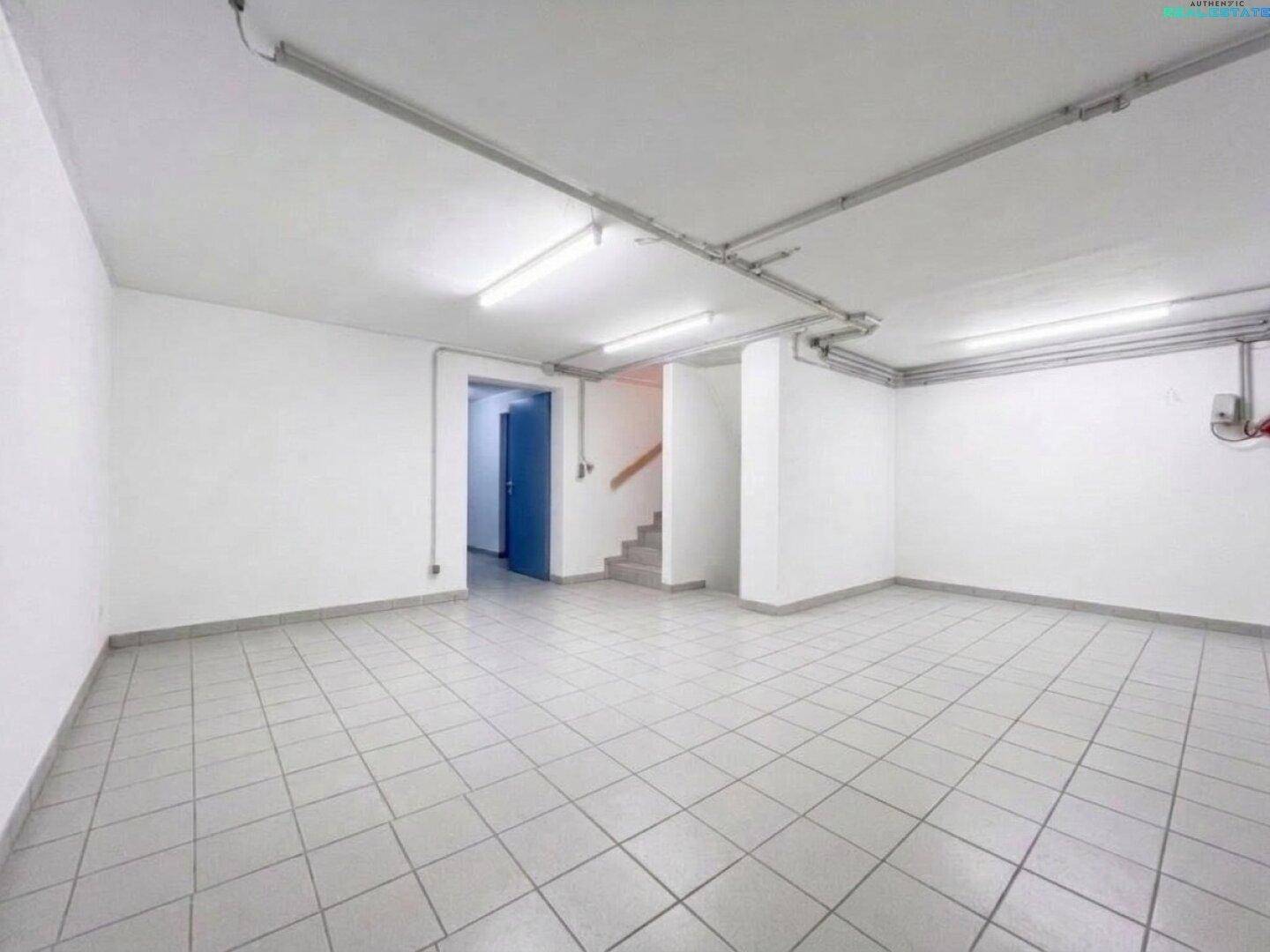 Geräumiger Kellerraum mit Fliesenboden, weißen Wänden und sichtbaren Leitungen an der Decke.