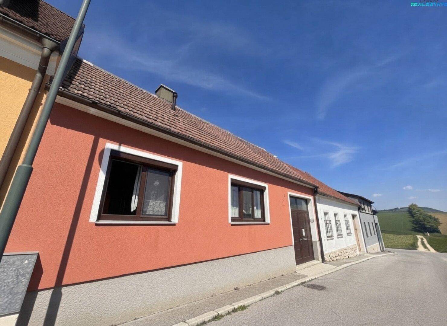 Traditionelles Haus mit orangeroter Fassade und braunen Fenstern an einer ländlichen Straße.