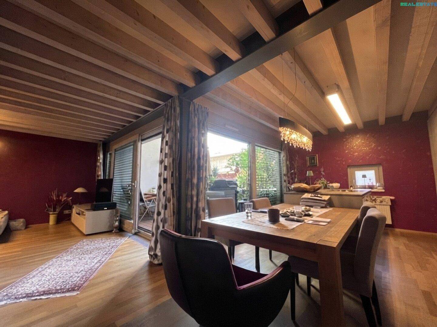 Heller offener Wohn- und Essbereich mit sichtbaren Holzbalken, Parkettboden und Zugang zur Terrasse.