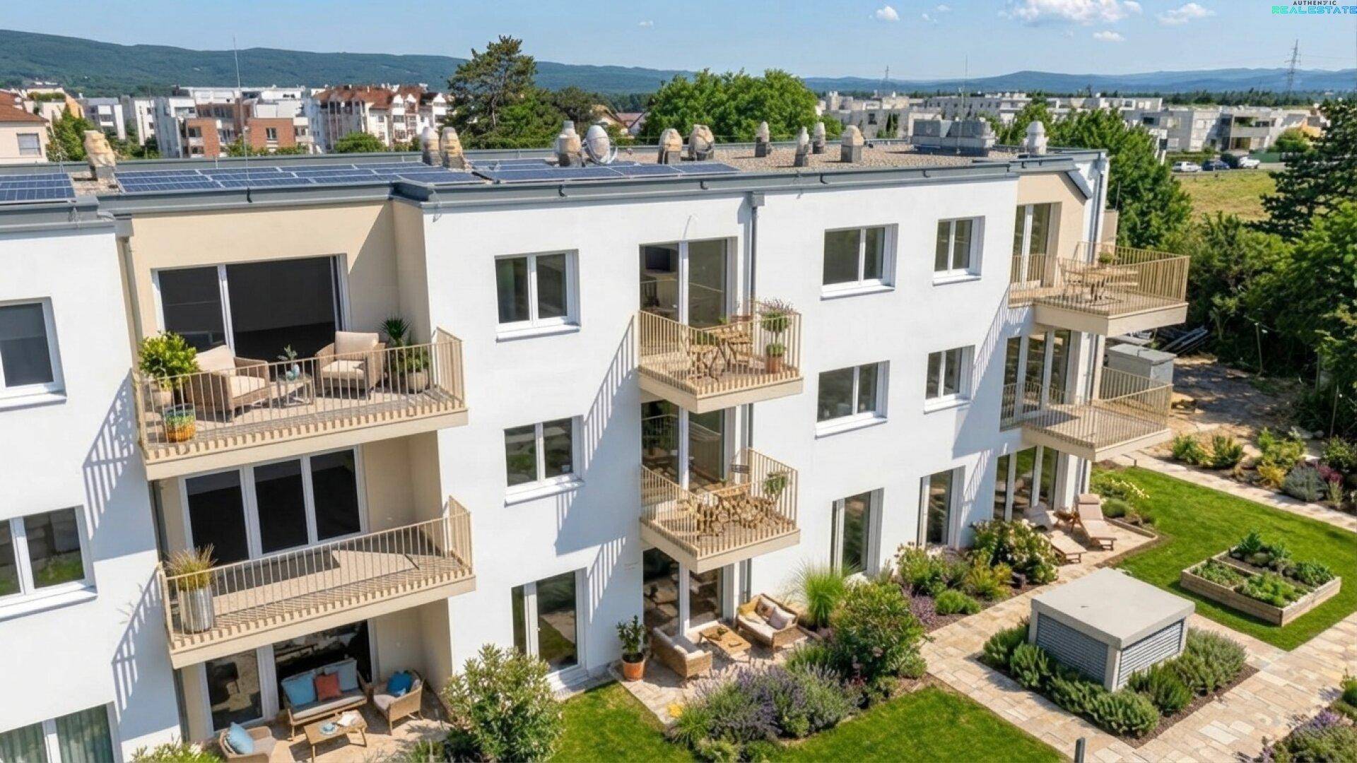 Luftaufnahme einer modernen Wohnanlage mit Balkonen, Gärten und Photovoltaikanlage auf dem Dach.