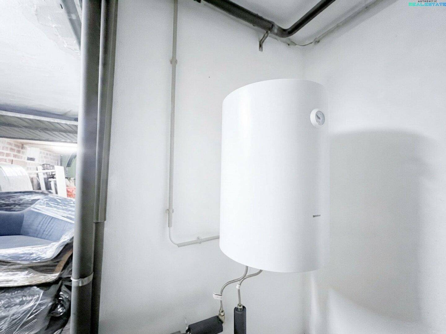 Hauswirtschaftsraum mit weißem Warmwasserboiler und sichtbaren Rohrleitungen an der Wand.