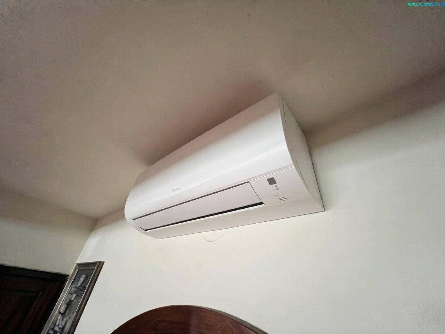 Weiße Klimaanlage an der Wand, über einem dunklen Möbelstück in einem Innenraum montiert.