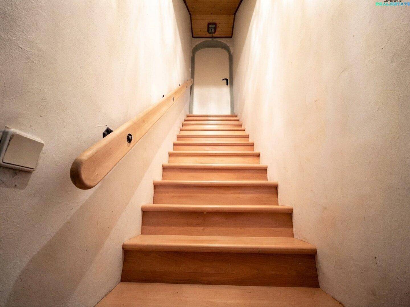 Holztreppe mit hellem Geländer und weißen Wänden führt nach oben.