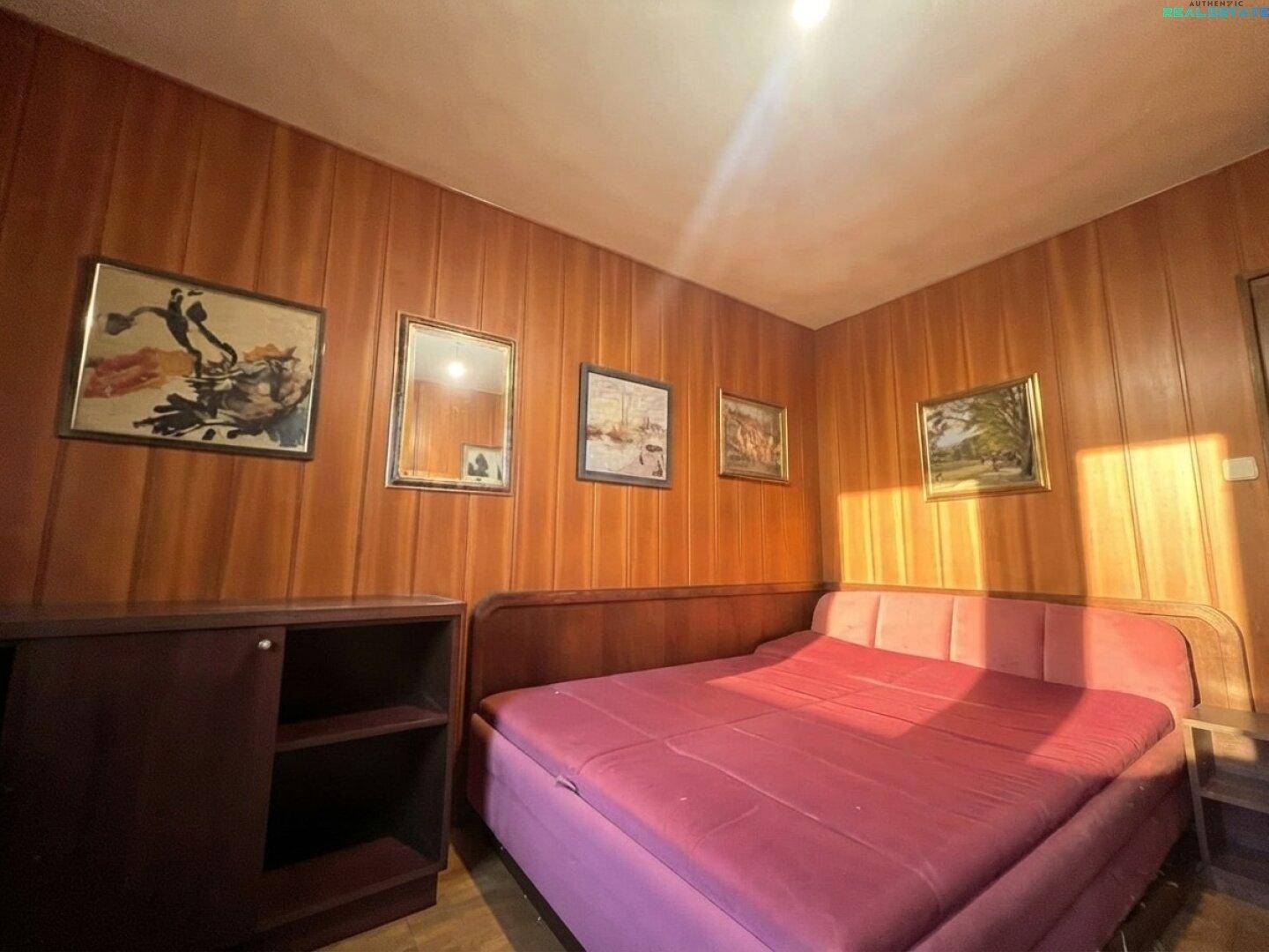 Schlafzimmer mit Holzvertäfelung, Bett und gerahmten Bildern an der Wand.