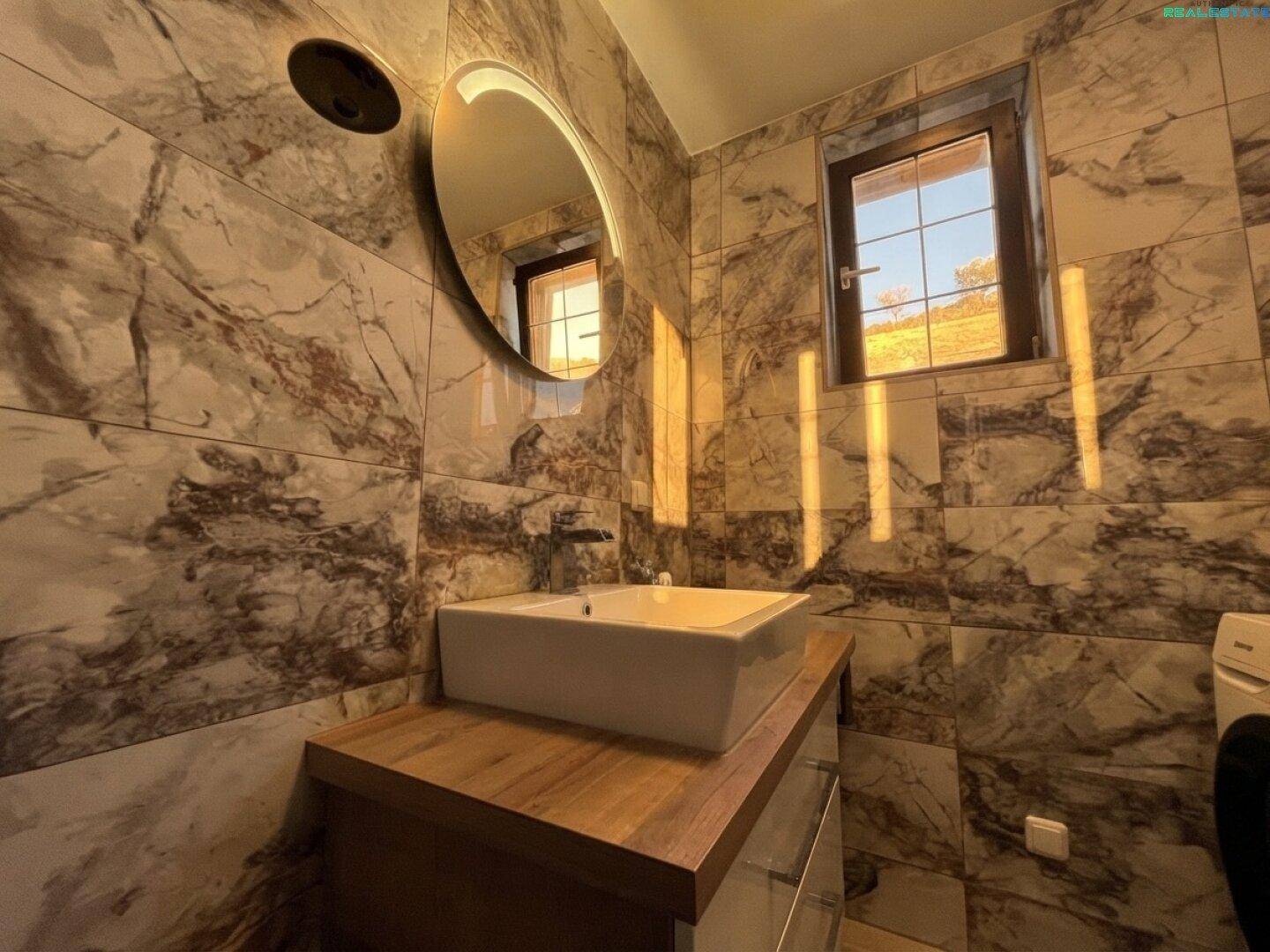 Modernes Badezimmer mit Marmoroptik-Fliesen, Aufsatzwaschbecken und beleuchtetem Spiegel.