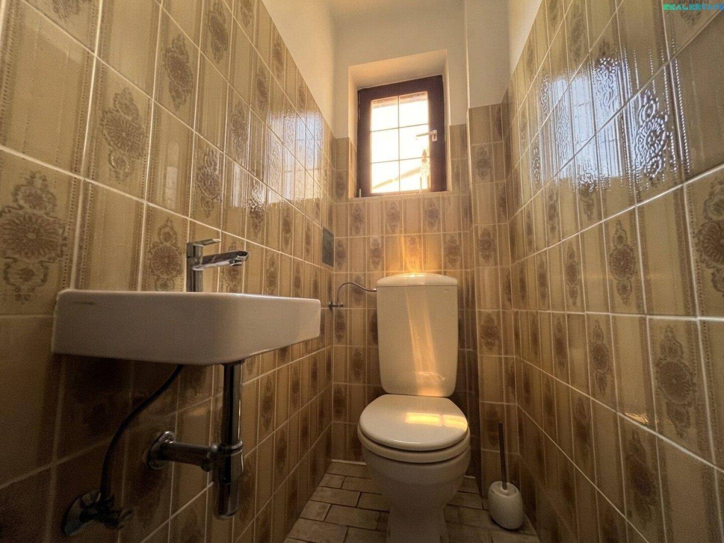 Kleines Gäste-WC mit gemusterten Fliesen, Toilette und Fenster.