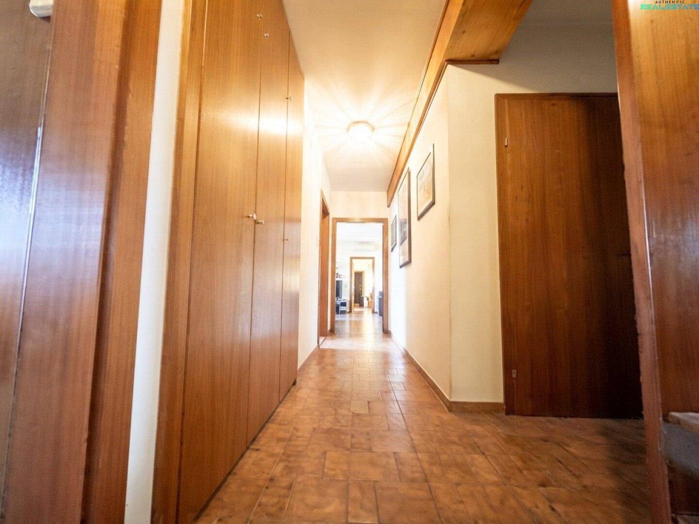 Langer Flur mit Einbauschränken aus Holz und Fliesenboden.