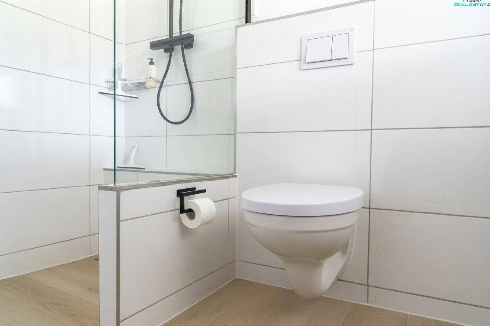 Modernes Badezimmer mit wandhängendem WC, Duschbereich und weißen Fliesen.