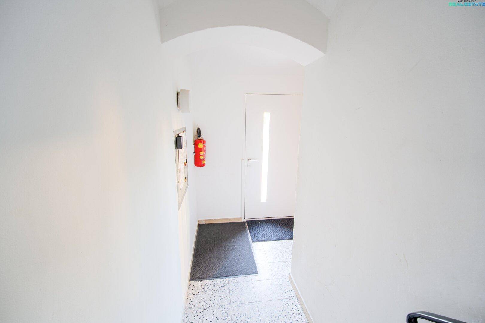 Heller Flur mit weißer Tür, Fußmatten und einem Feuerlöscher an der Wand, sicher und ordentlich.