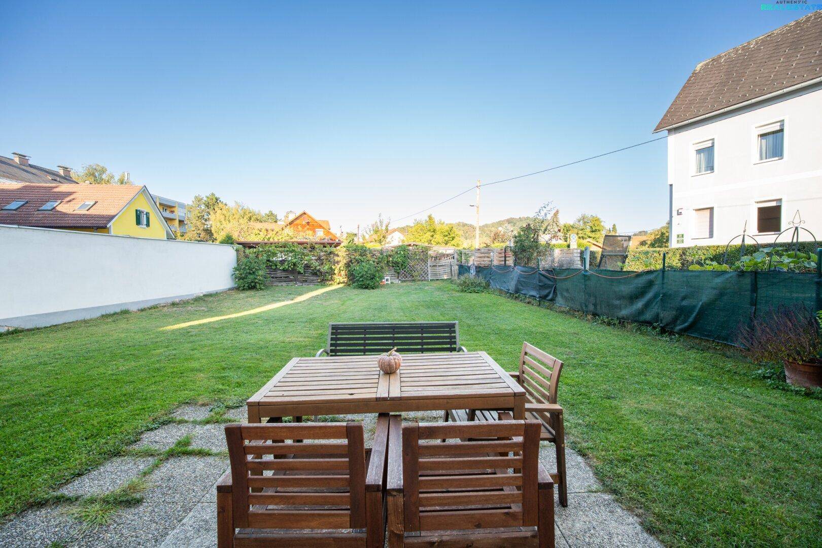 Großer, gepflegter Garten mit Rasenfläche und Holzmöbeln für den Außenbereich, ideal zum Entspannen.