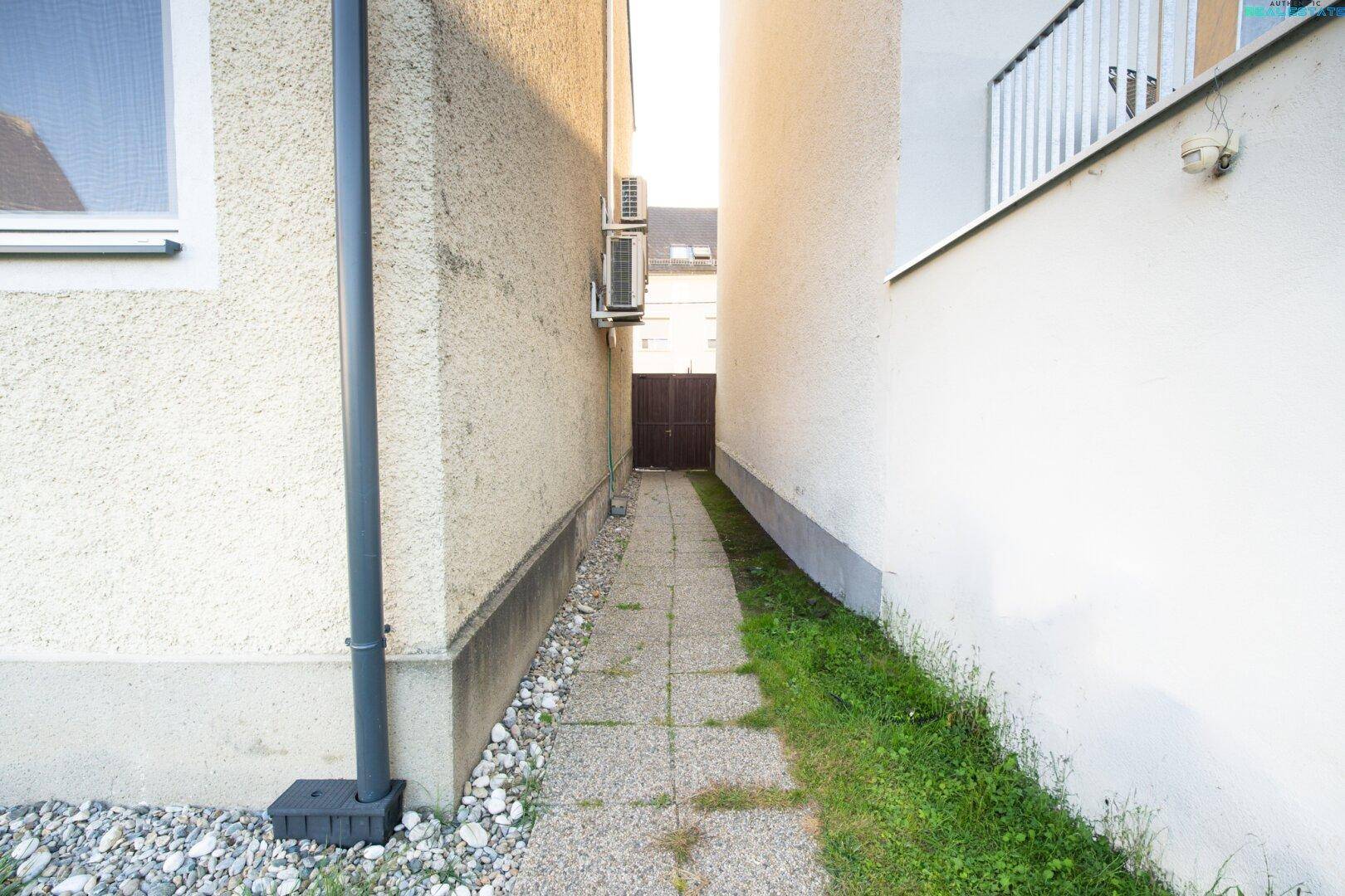 Schmaler Zugangsweg zwischen zwei Gebäuden, führt zu einem Tor im hinteren Bereich des Grundstücks.